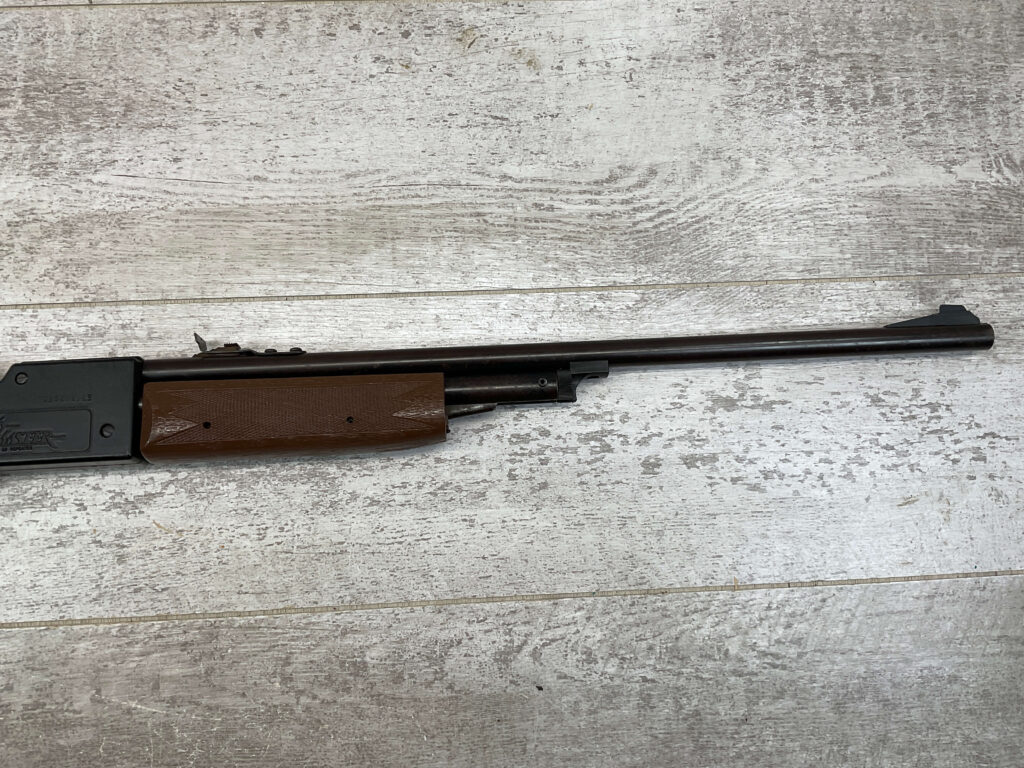 Air rifle with wooden stock, used for shooting practice or sport, placed on a wooden surfaceâ€”highlighting outdoor activity or hunting gear at Checkpoint Charlie's.