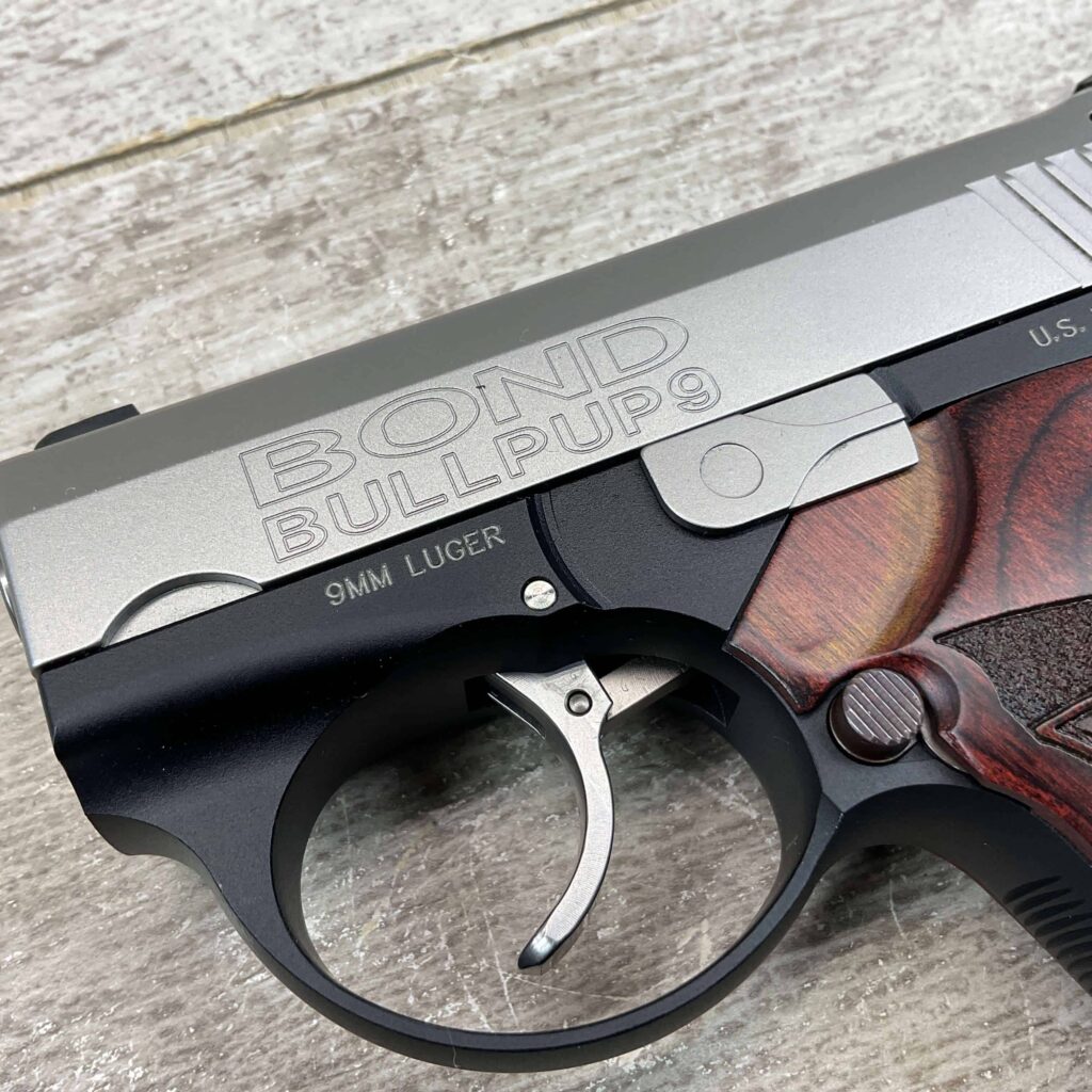 9mm handgun with "BOND BULLPUP 9" engraved, featuring a stainless steel slide and wooden grip, positioned on a wooden surface.